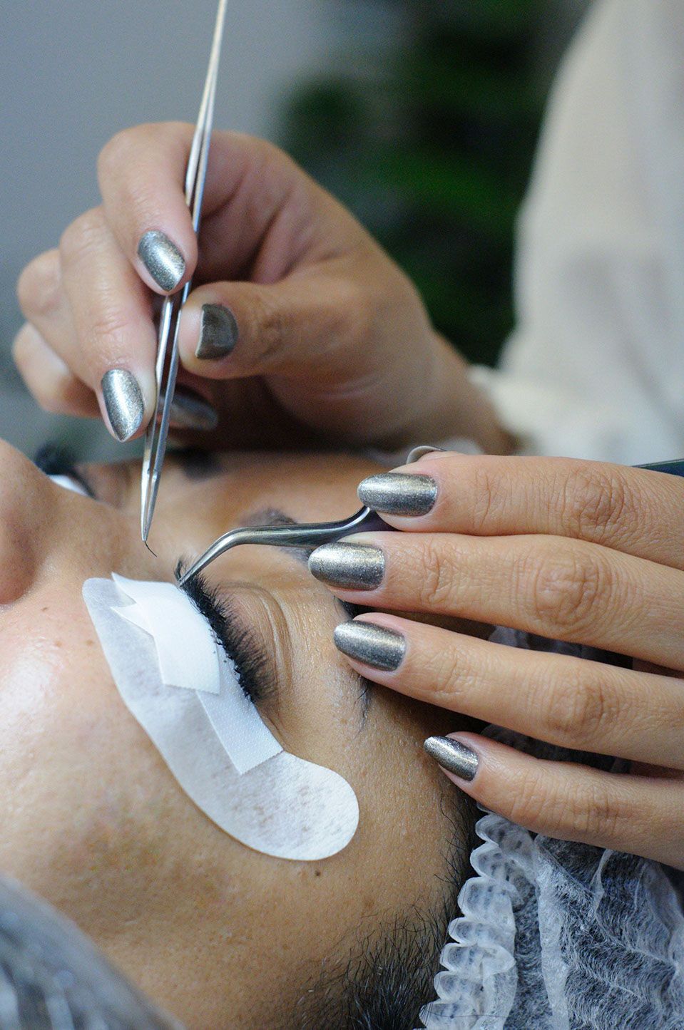 Person getting eyelash extensions applied with tweezers.
