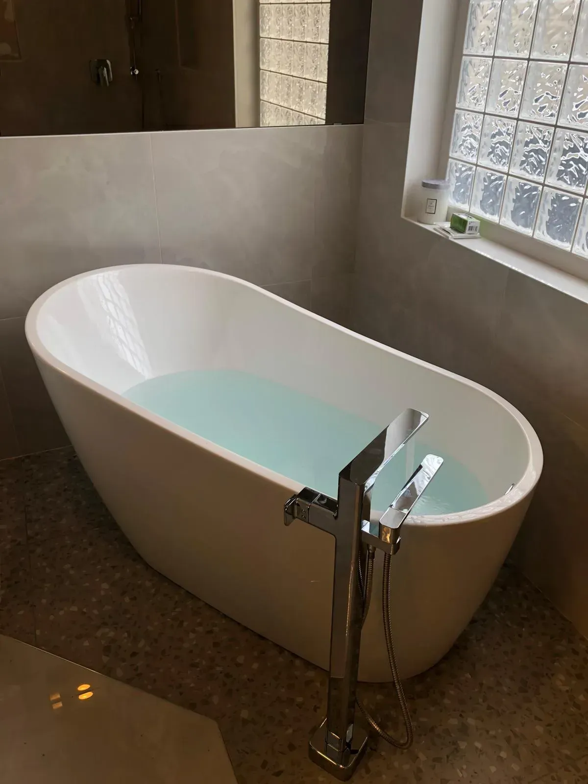 A bathtub filled with blue water in a bathroom next to a window.