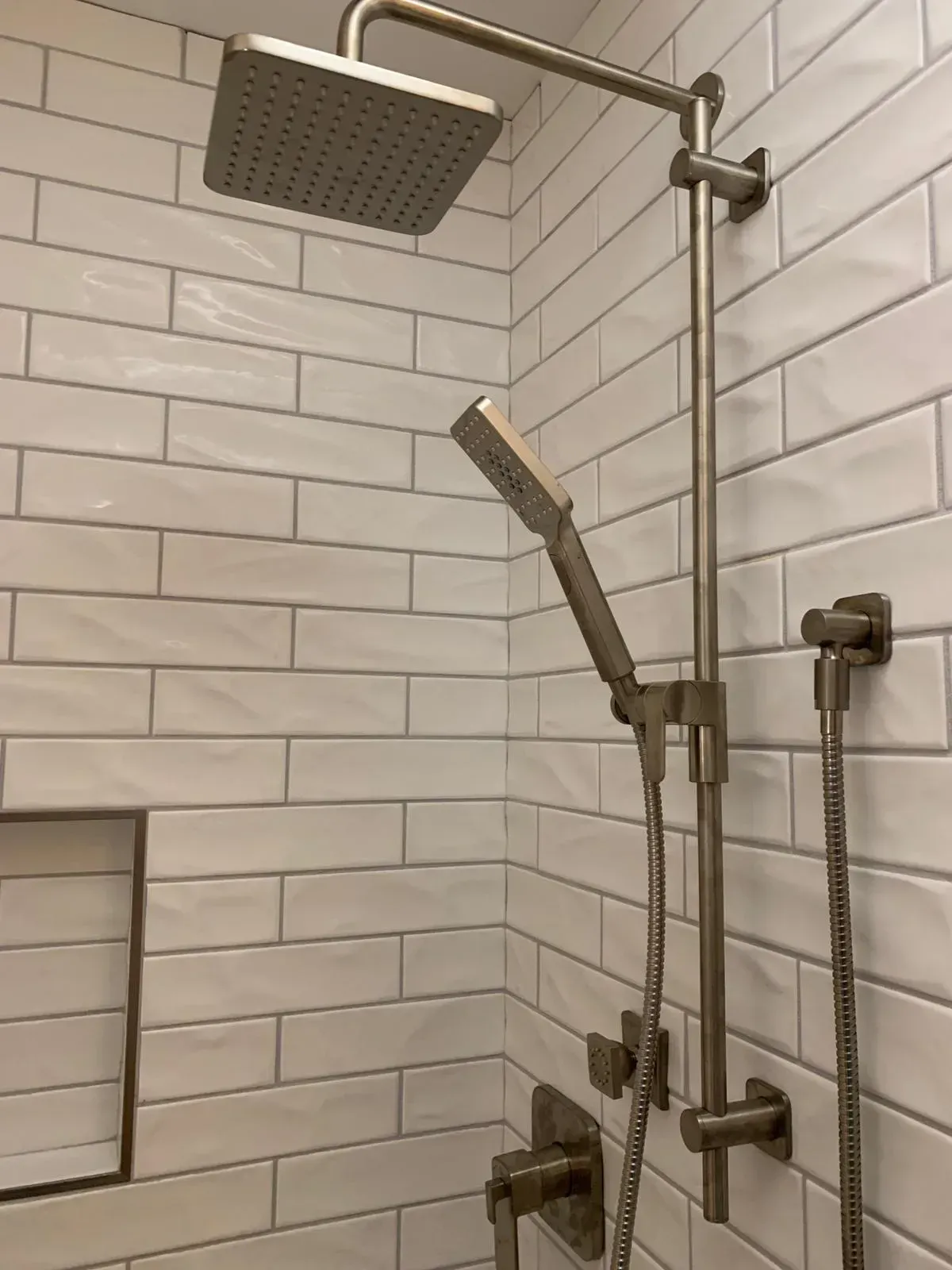 A shower head is mounted to a white brick wall in a bathroom.