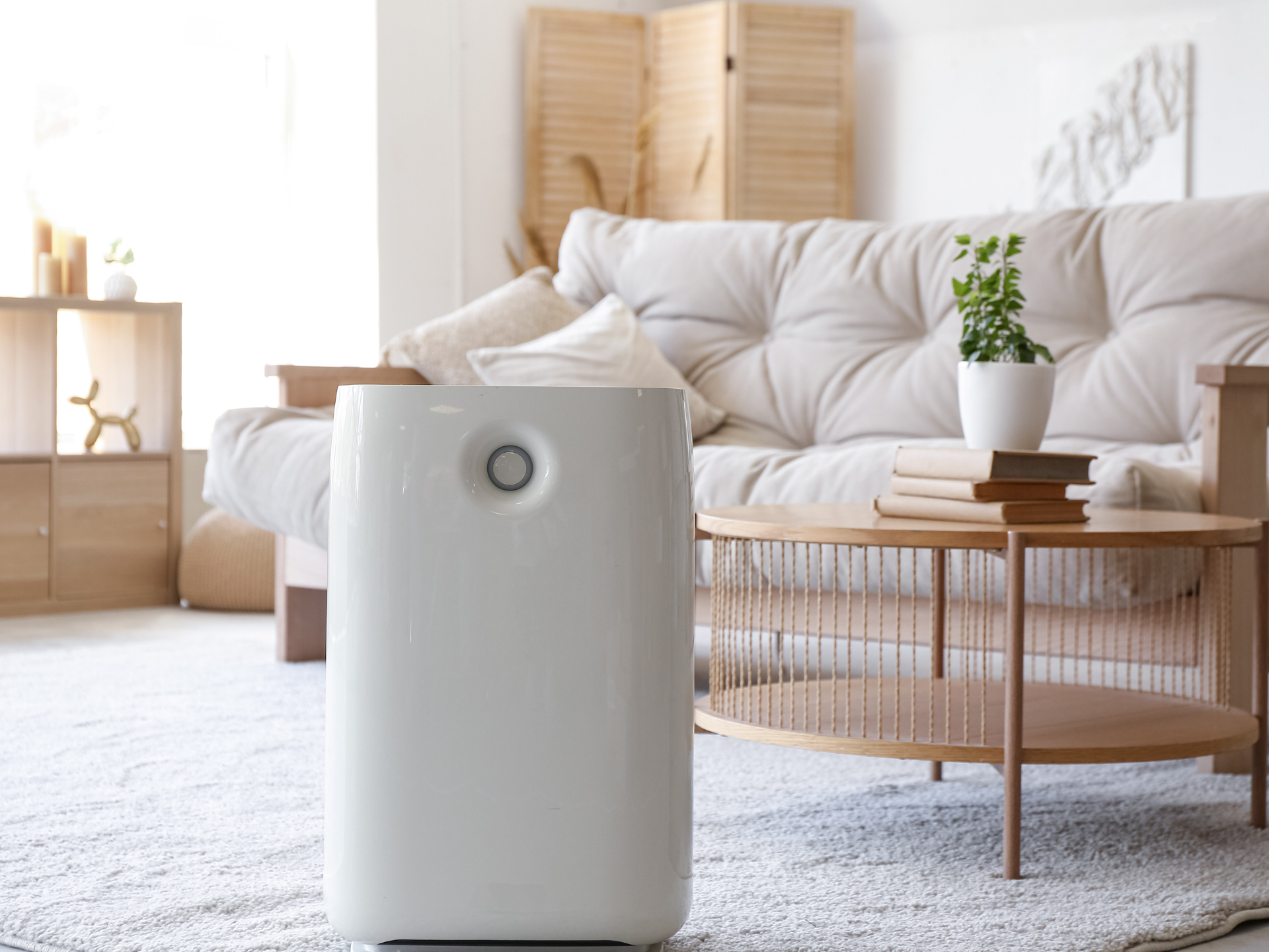 White air purifier in a cozy living room with a beige couch and wooden coffee table.