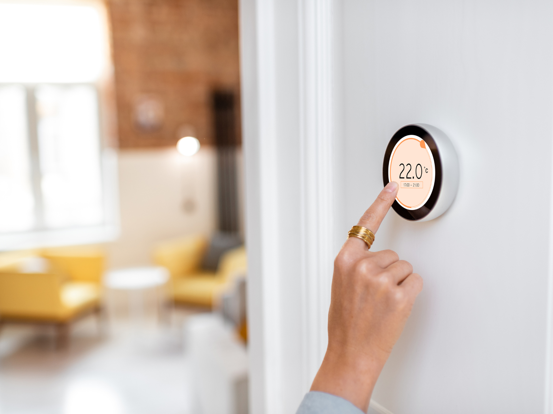 Hand adjusting a smart thermostat showing 22 degrees on a white wall in a living room.