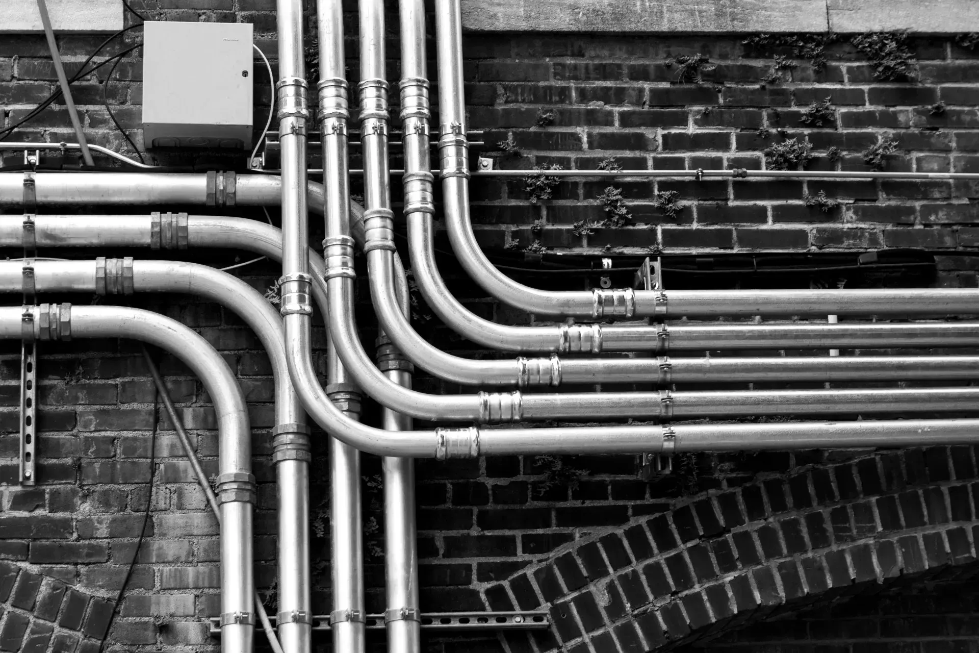 A black and white photo of a bunch of pipes on a brick wall.