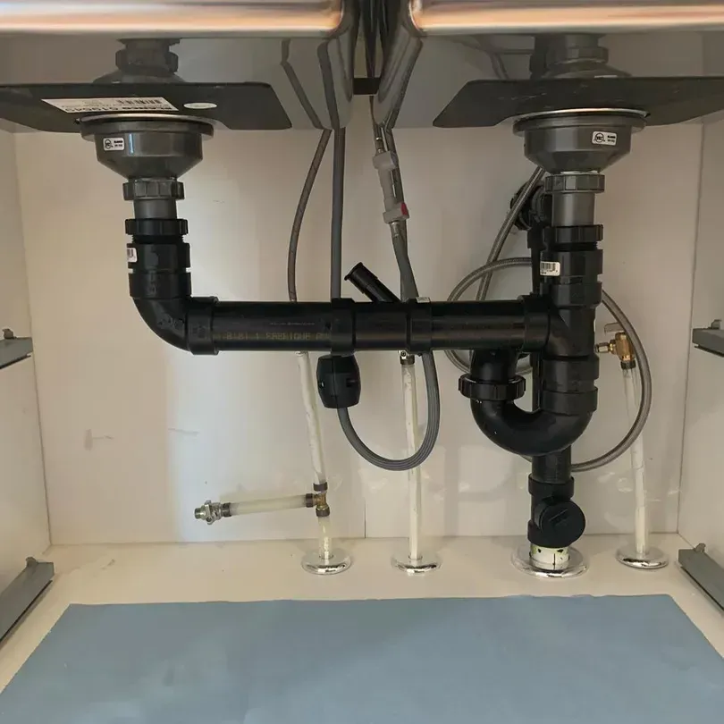 Underneath a kitchen sink there are many pipes and wires