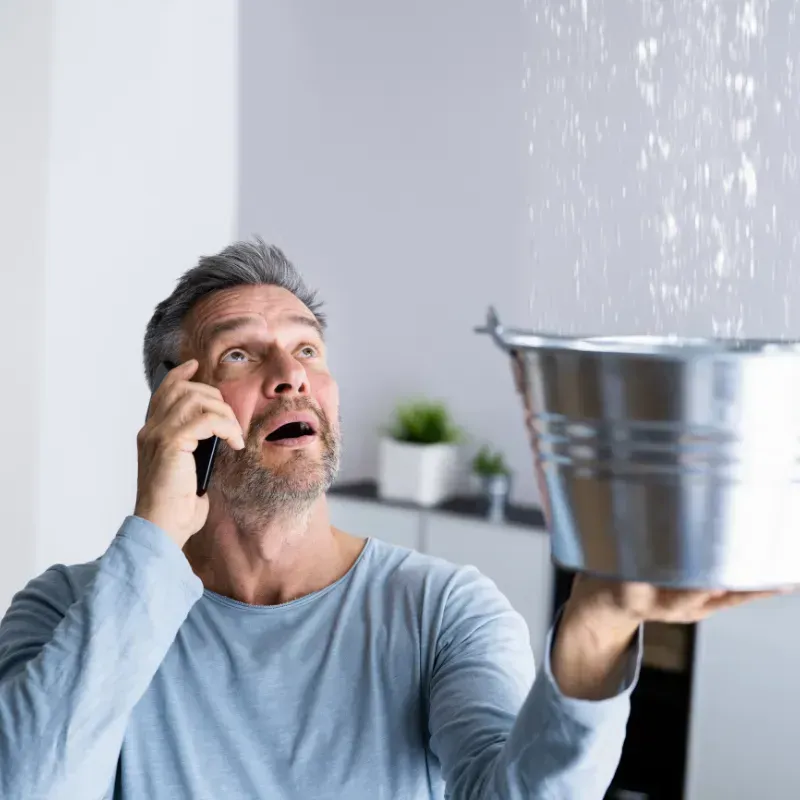 A man is talking on a cell phone while holding a bucket.