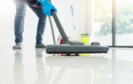 Housekeeping and housework cleaning concept, Happy young man in blue rubber gloves using a vacuum cleaner on floor at home.