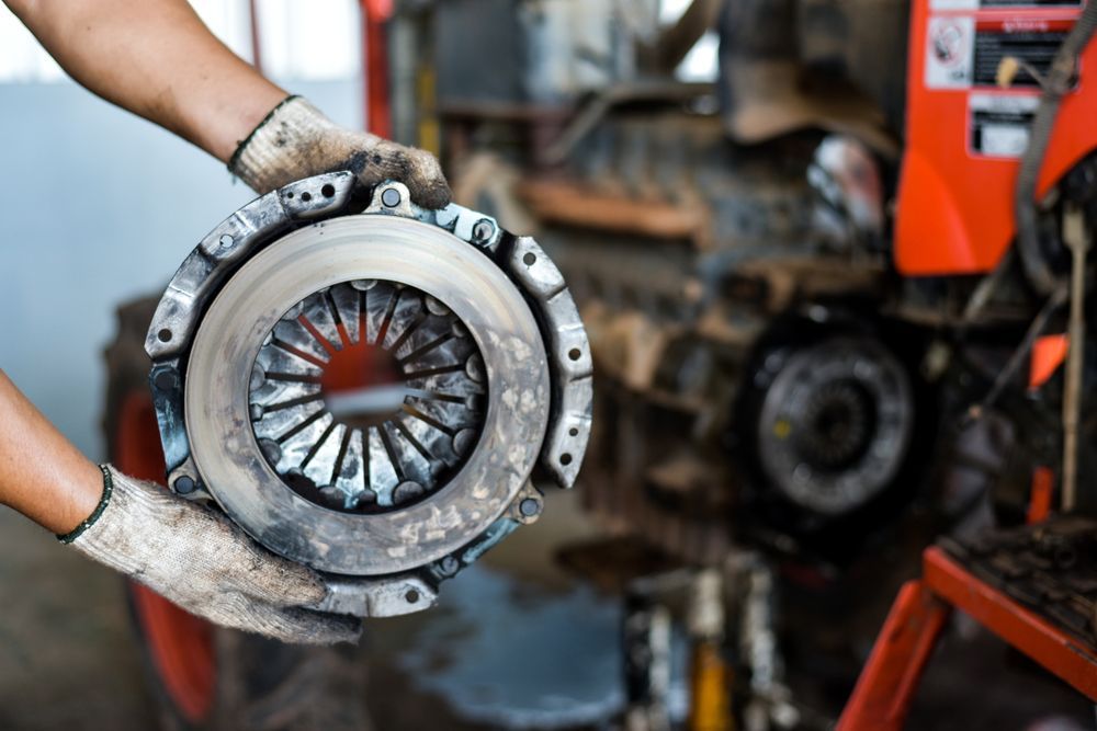 Man Holding A Clutch Plate In Their Hands In Front Of A Tractor — Tamworth Manual Transmission Factory In Tamworth, NSW