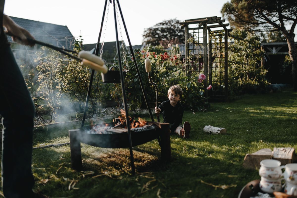 Iemand die een vuur stookt in een achtertuin met rook, bloemen en tuinmeubilair.
