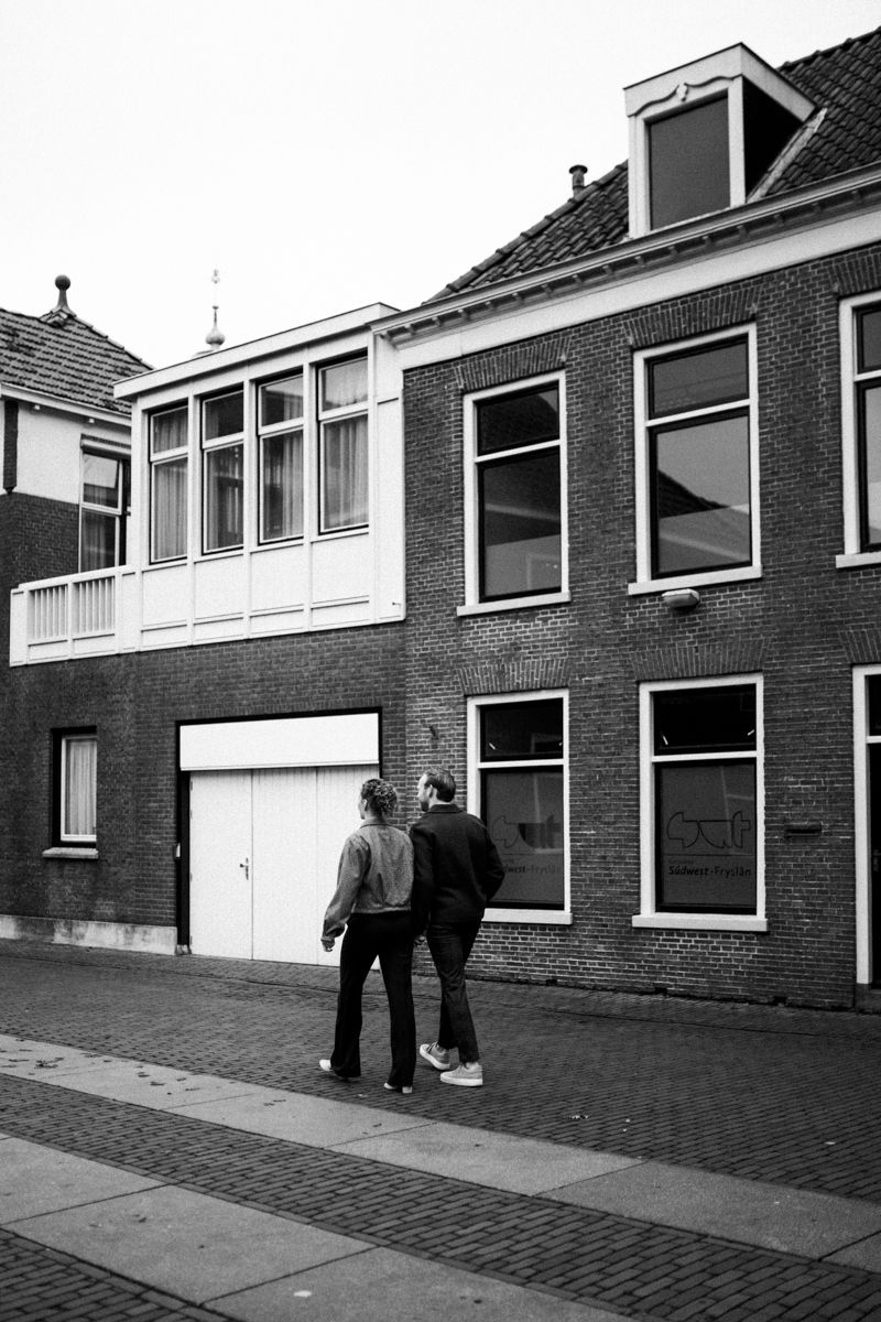 Een persoon in een wit shirt strooit ingrediënten over een kleine taart op een aanrecht vol schalen en peren.