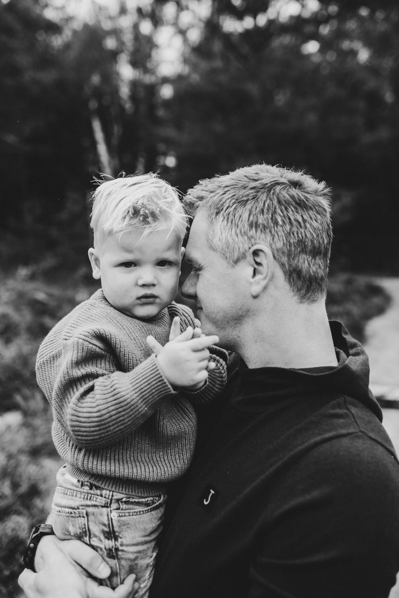 Een zwart-witportret van een volwassene die een jong kind buiten vasthoudt; beiden kijken naar de camera.