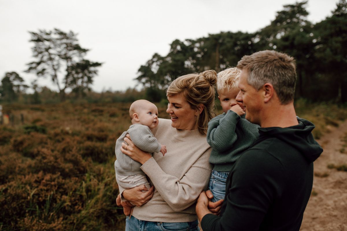 Een gezin van vier personen zit buiten in een veld, lachend en hun kinderen vasthoudend, terwijl ze casual kleding dragen.
