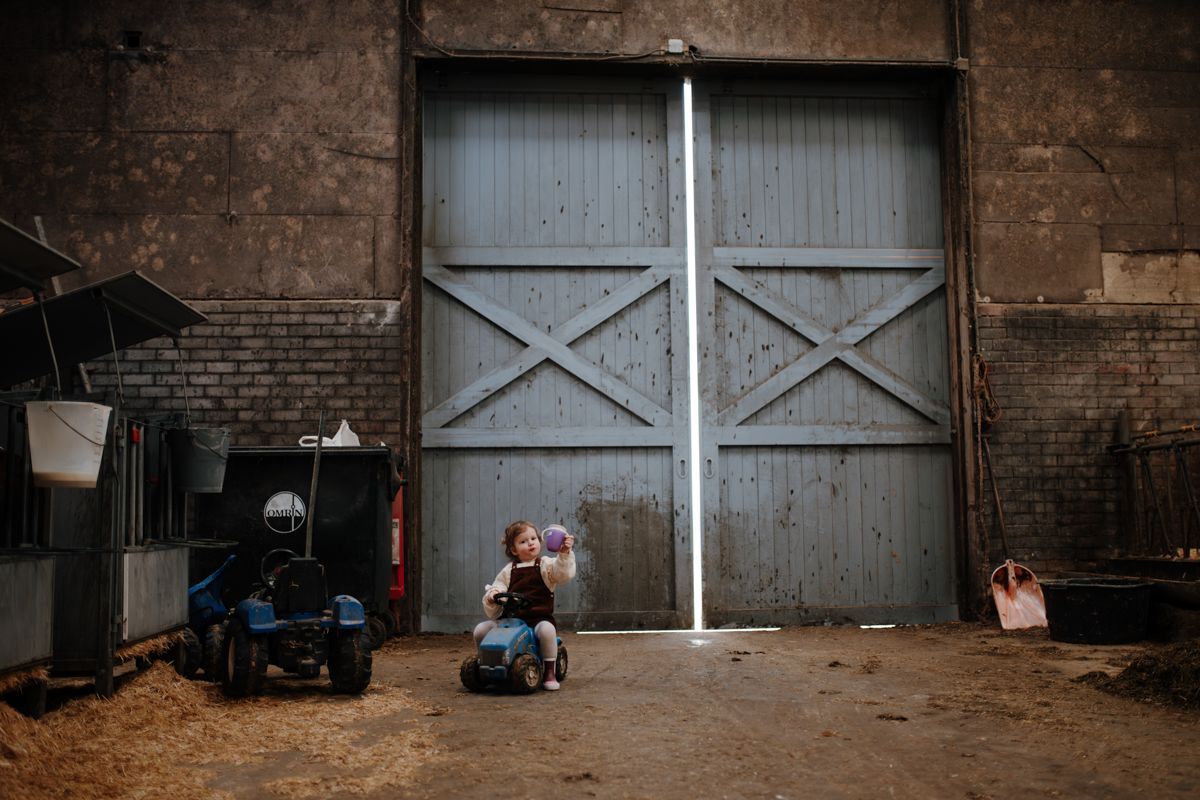 Meisje op speelgoedtractor voor de boerderijstal, gezinsshoot Friesland – Froukje Kuiper Fotografie