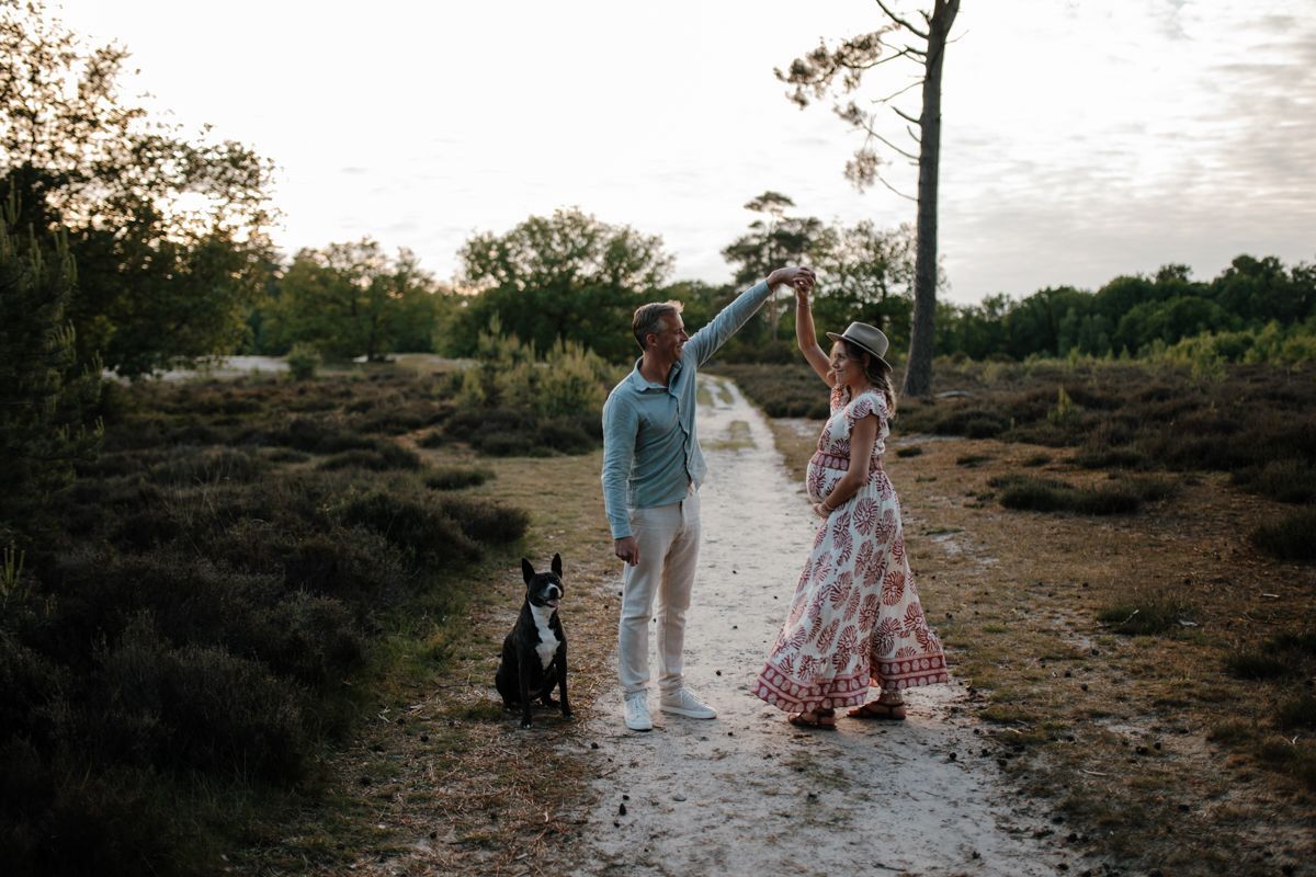 Zwanger stel doet een dansje tijdens de fotoshoot en de hond zit ernaast