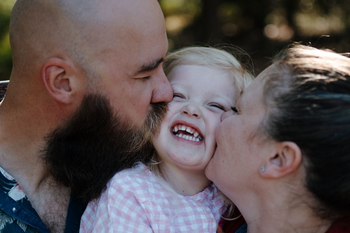 Vader en moeder geven kindje een kus op de wang tijdens een fotoshoot