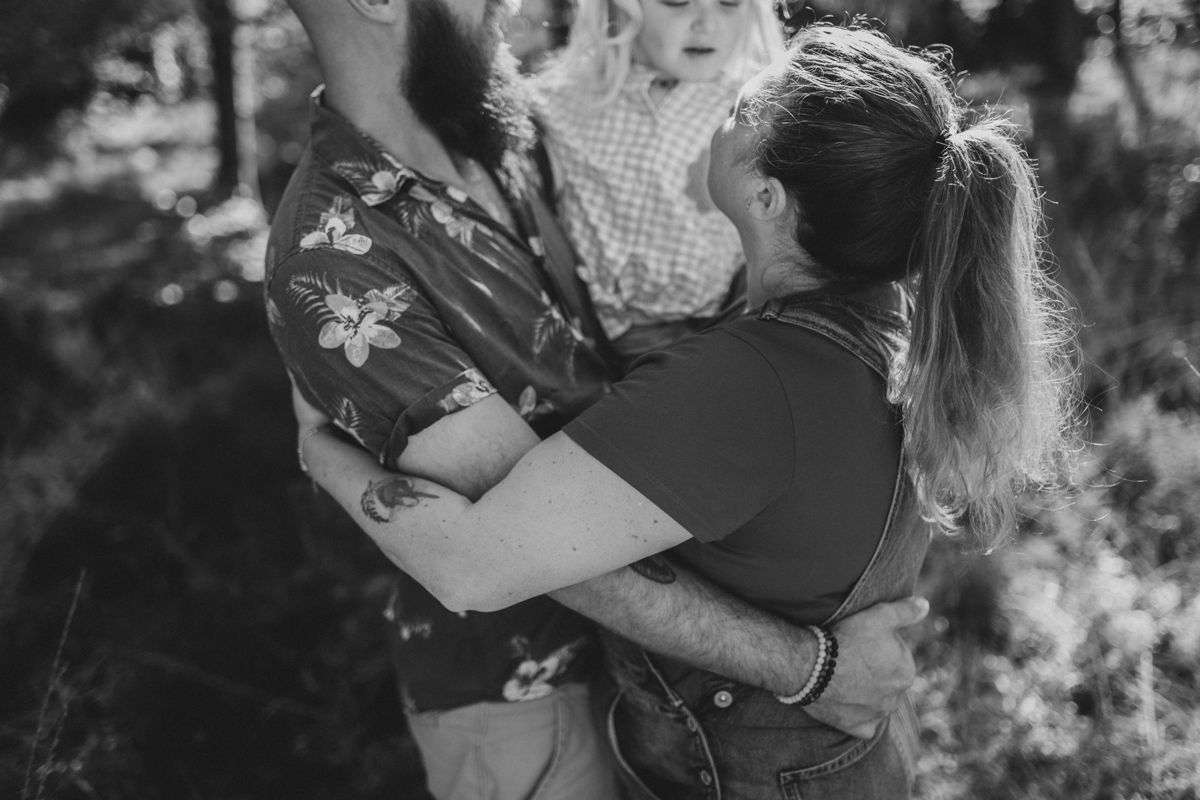 Een stel omhelst elkaar in de buitenlucht terwijl ze een kind vasthouden, vastgelegd op een zwart-witfoto.