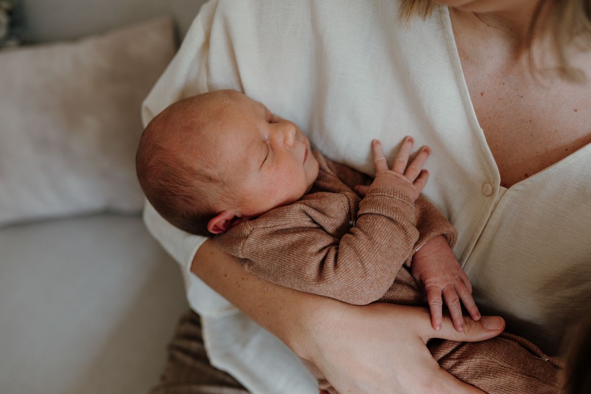 Een slapende baby wordt dicht tegen zich aan gehouden in de armen van een vrouw, tijdens een newbornshoot in Drenthe
