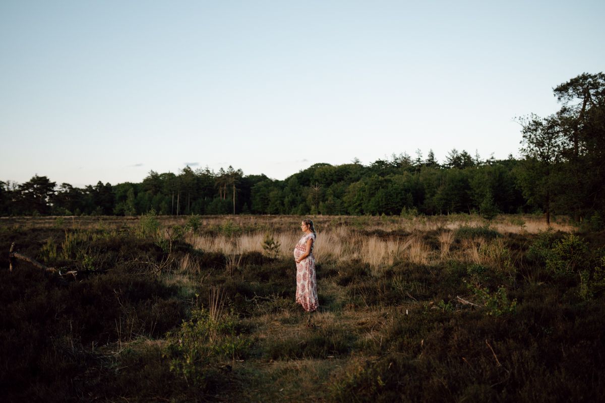 Zwangere vrouw tijdens de fotoshoot met een mooie zonsondergang en rood witte jurk aan in de natuur van Bakkeveen