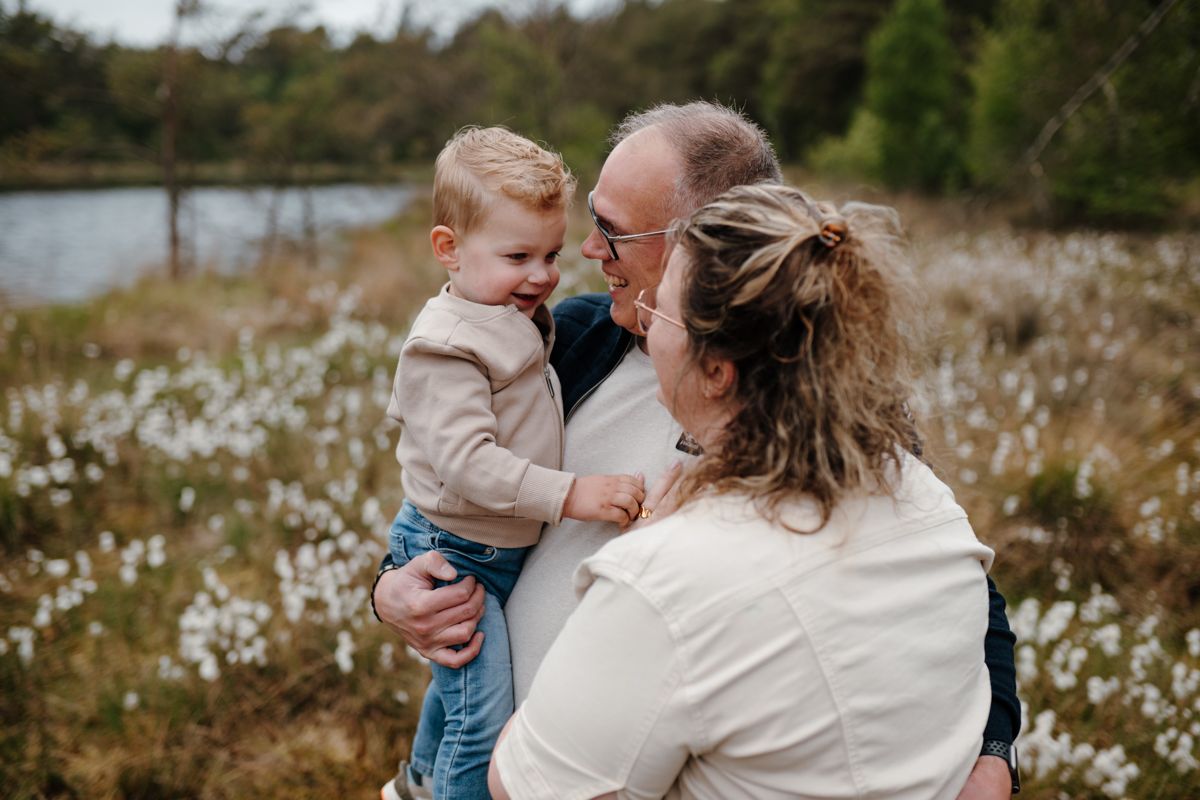 Peuter wordt opgetild door vader en moeder tijdens een fotoshoot in de natuur