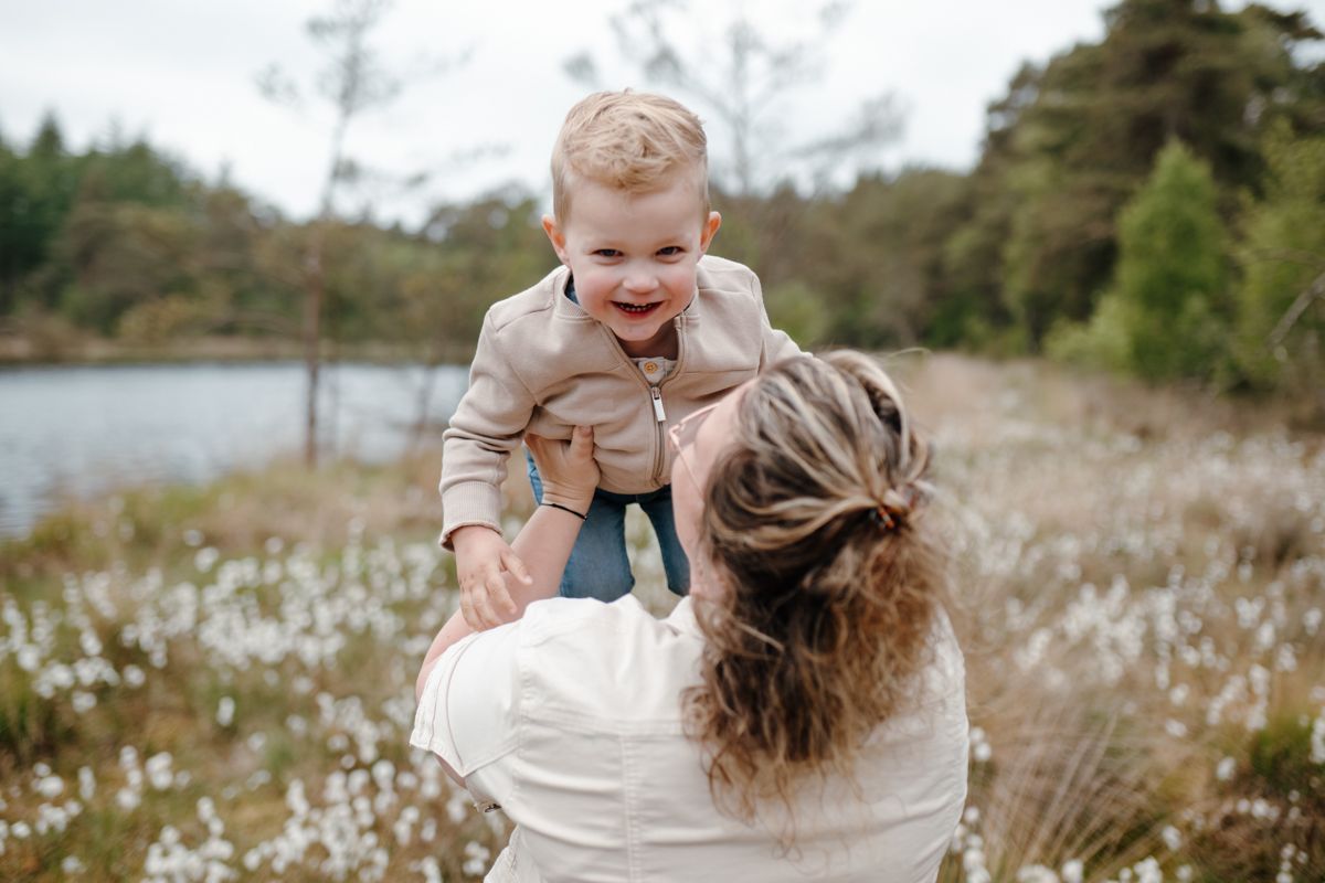 Moeder tilt haar kindje op tijdens een fotoshoot in het bos