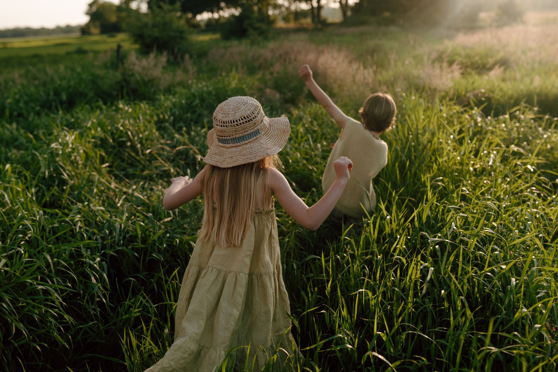 Broer en zus wandelen door het hoge gras tijdens een fotoshoot van hun gezin in de natuur