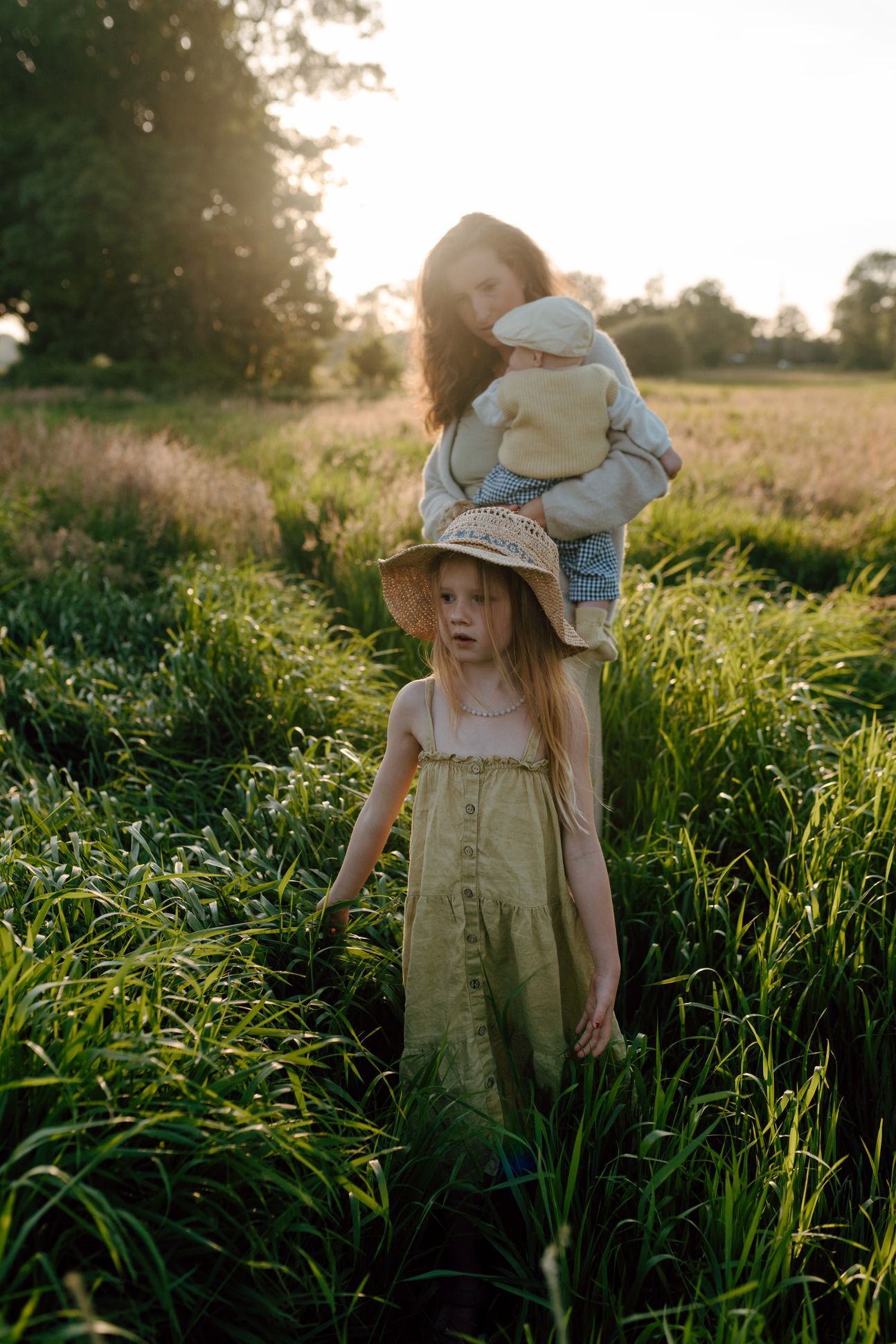 Moeder met twee kinderen in het hoge gras aan het wandelen tijdens een gezinsshoot