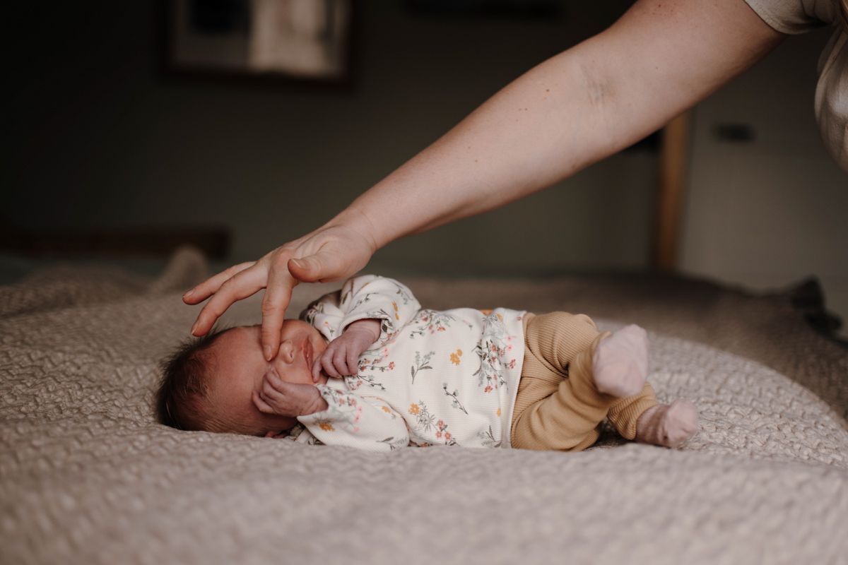 Newborn shoot thuis, baby ligt op het grote bed en gaat slapen
