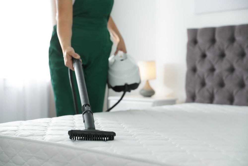 Person in Green Cleaning a Mattress With a Steam Cleaner in a Bedroom — Citrus Clean Central Coast In Lake Haven, NSW