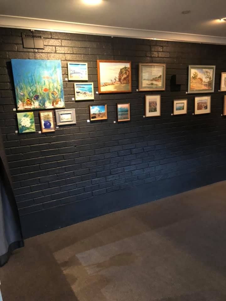 An art gallery wall featuring numerous framed paintings displayed on a painted black brick surface.