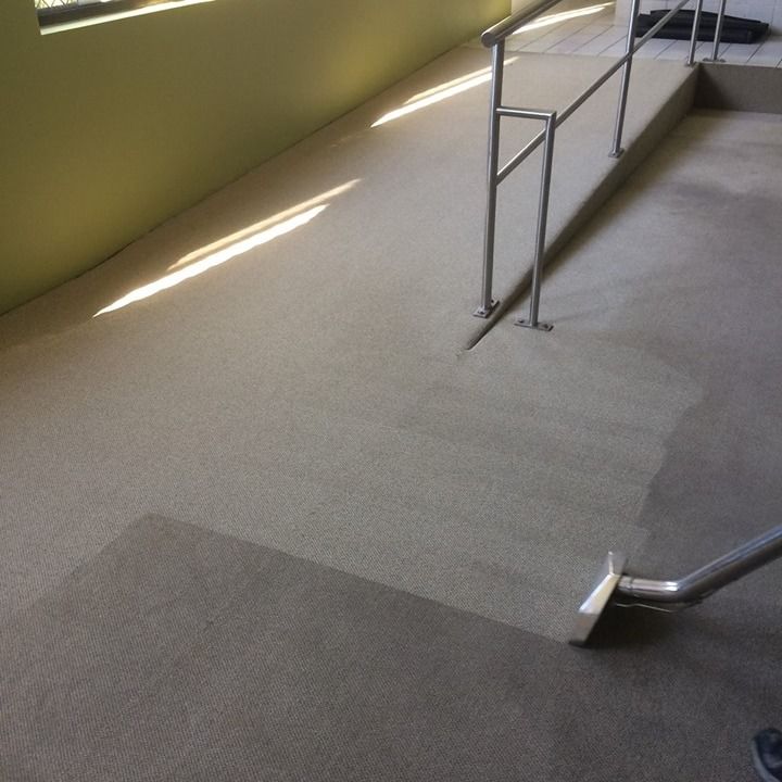 A carpet cleaning wand cleans a strip of beige carpet on a ramp next to a metal railing.
