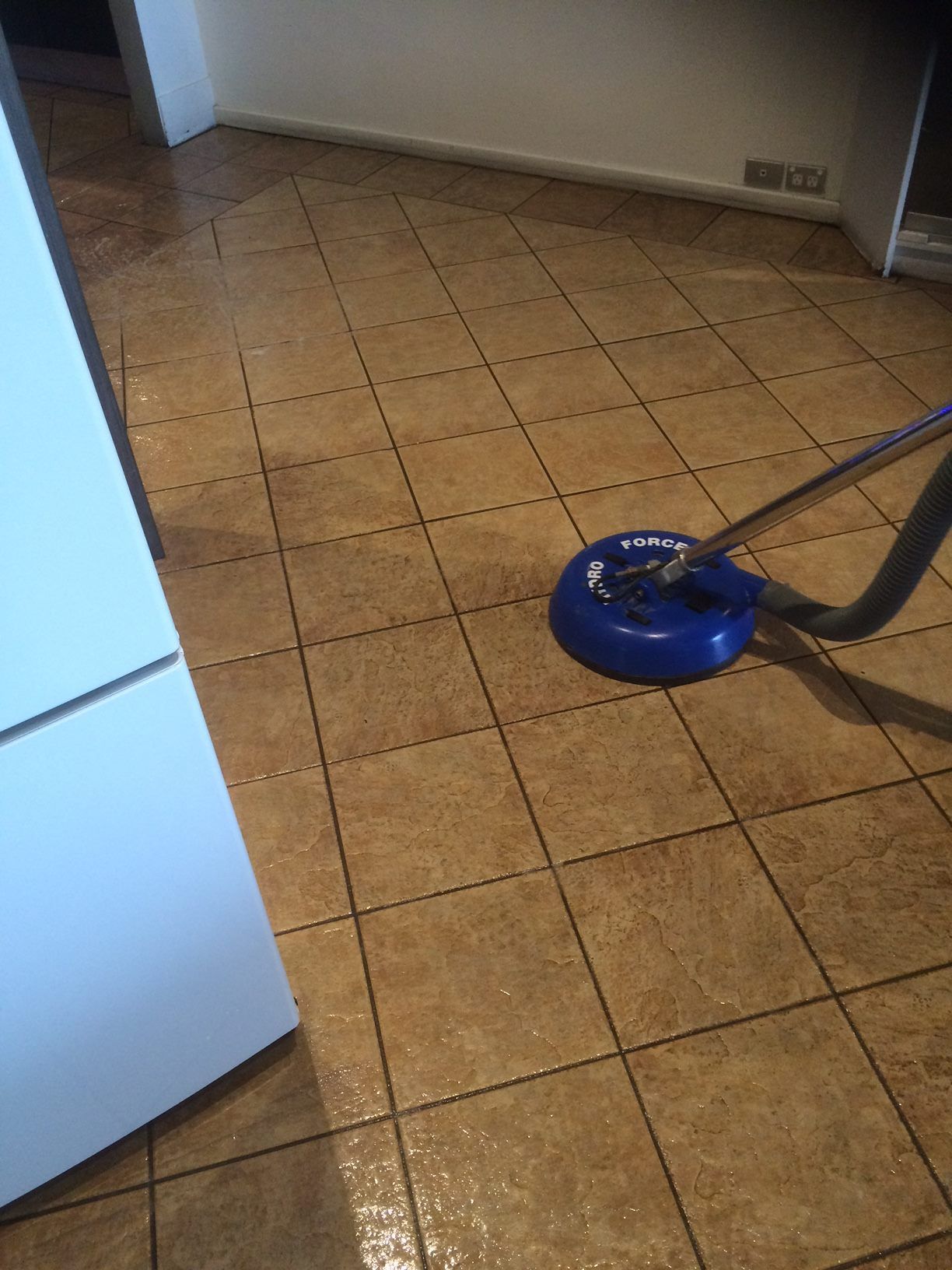 A blue floor-cleaning tool is being used to deep-clean a tiled floor, showing a distinct clean path against dirty tiles.