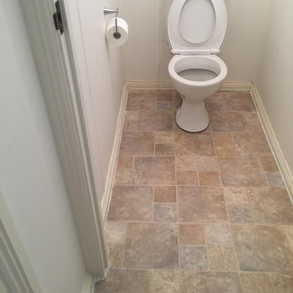 A view of a small bathroom featuring a white toilet on a tan and grey tiled floor with a toilet paper holder on the wall.