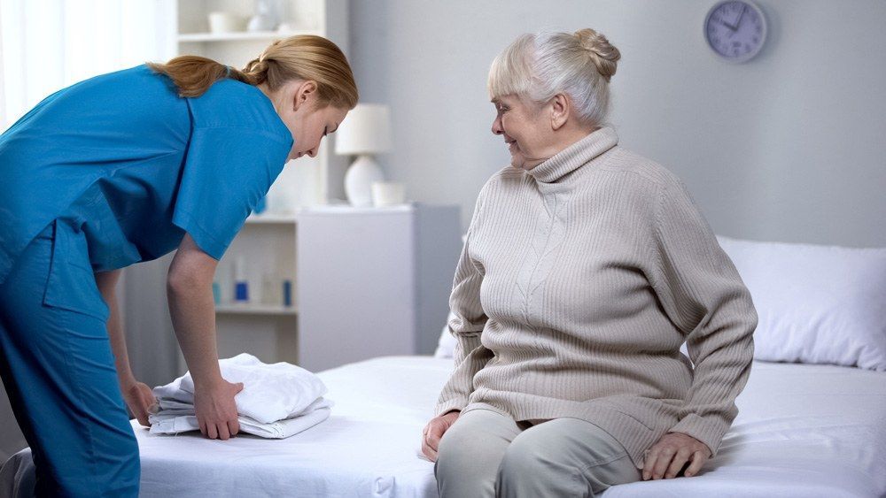 A Nurse Is Helping An Elderly Woman Get Out Of Bed — Citrus Clean Central Coast In Lake Haven, NSW