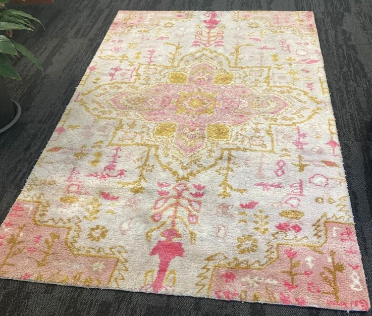 An area rug with a faded, ornate Persian-style pattern in soft pinks and muted yellows on a white background.