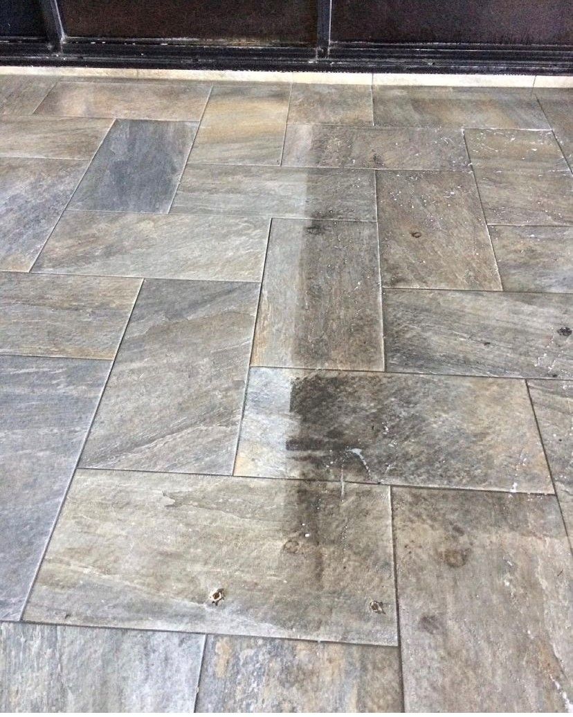 A stone tiled patio with a vertical line showing a dramatic difference between clean, light tiles and dirty, dark tiles.