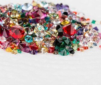 Pile of colorful, faceted gemstones: red, green, blue, purple, yellow, and clear.