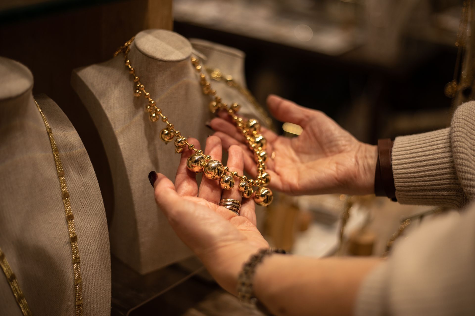 Hands holding a gold necklace in front of display busts.