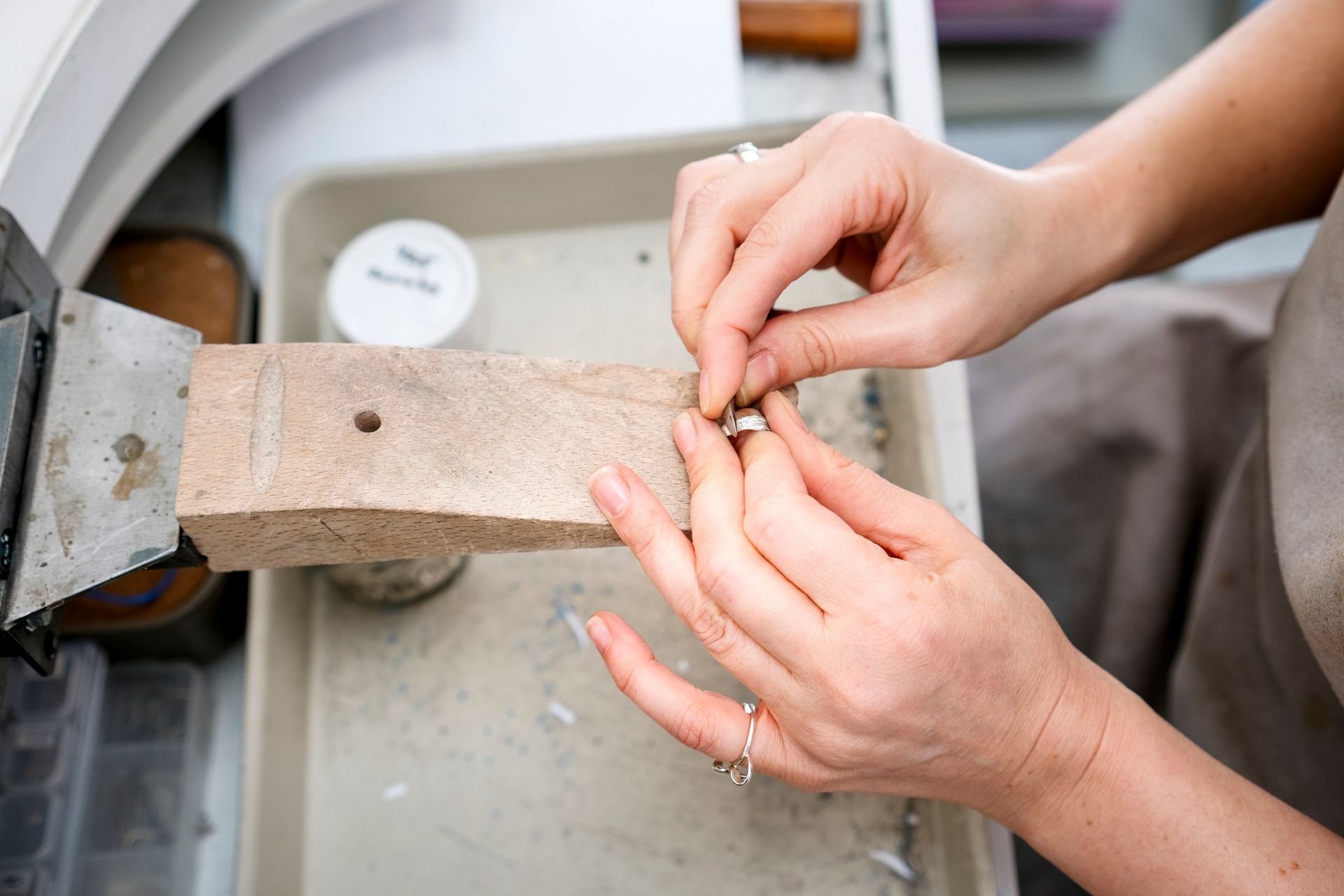 Jeweler works on silver ring at bench with tools and labeled tray. Jeweler works on silver ring at bench with tools and labeled tray.