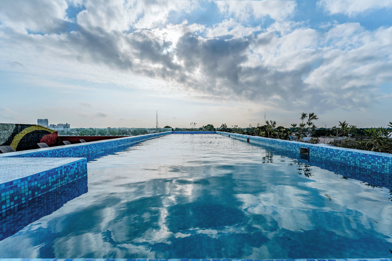 La piscina de la azotea refleja el cielo nublado; está rodeada de mosaicos azules.