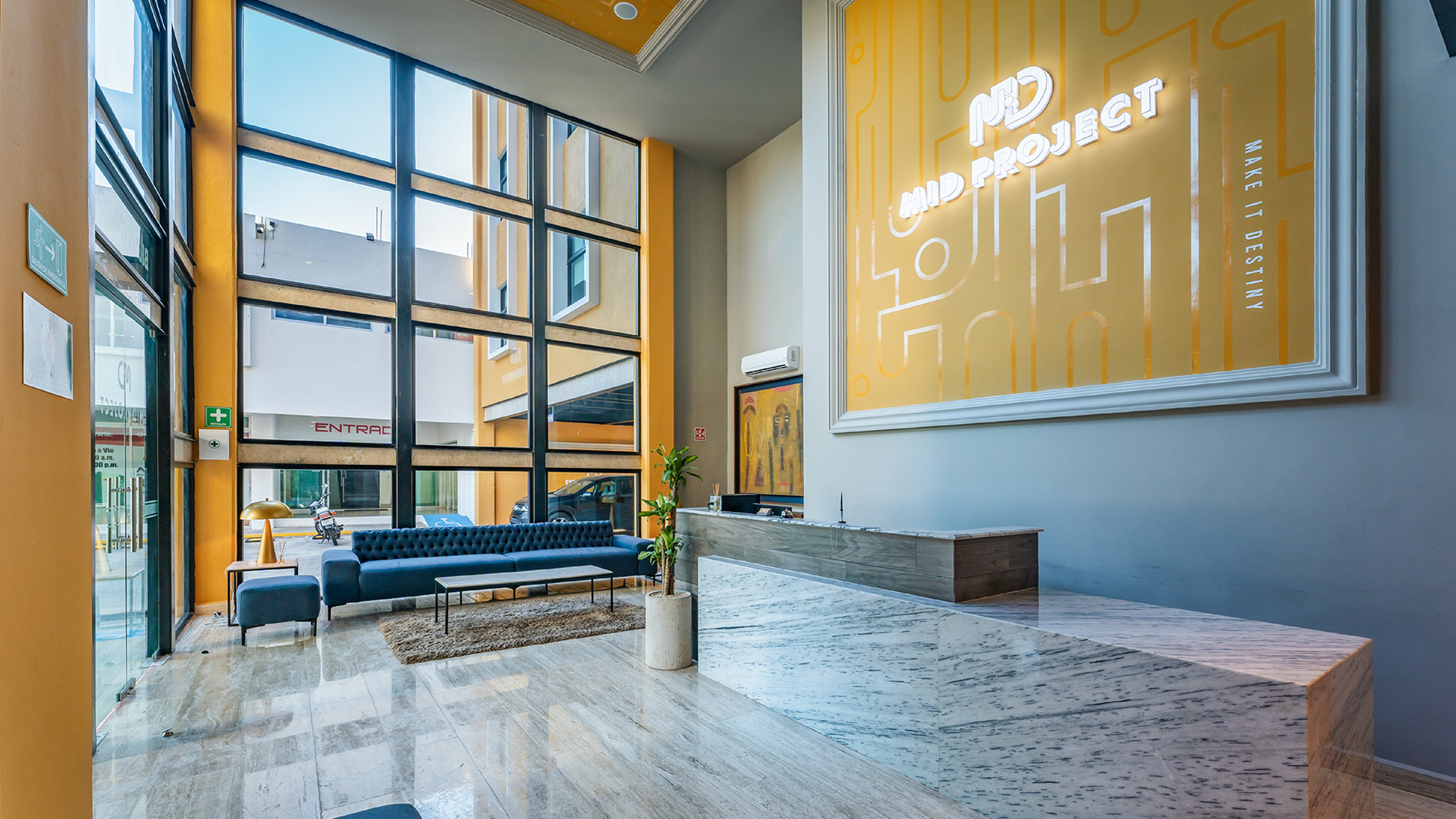 Vestíbulo con amplios ventanales, suelo de mármol, sofá y mostrador de recepción. Un cartel dice "Proyecto MD".