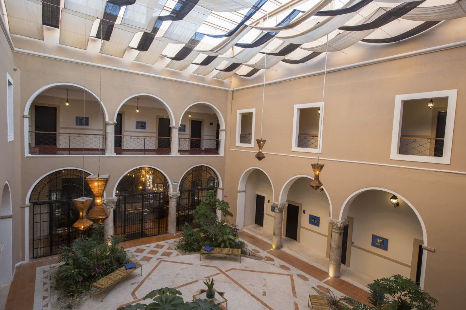 Patio interior con portales arqueados, balcones y un tejado parcialmente a dosel. Se aprecian plantas.