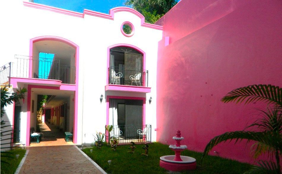 Edificio de estuco rosa con arcos, balcones y un patio con fuente.