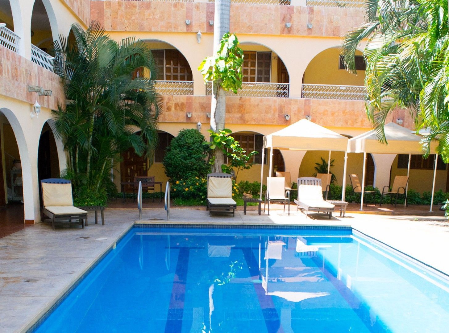 Piscina en el patio de un hotel, con tumbonas y asientos a la sombra.
