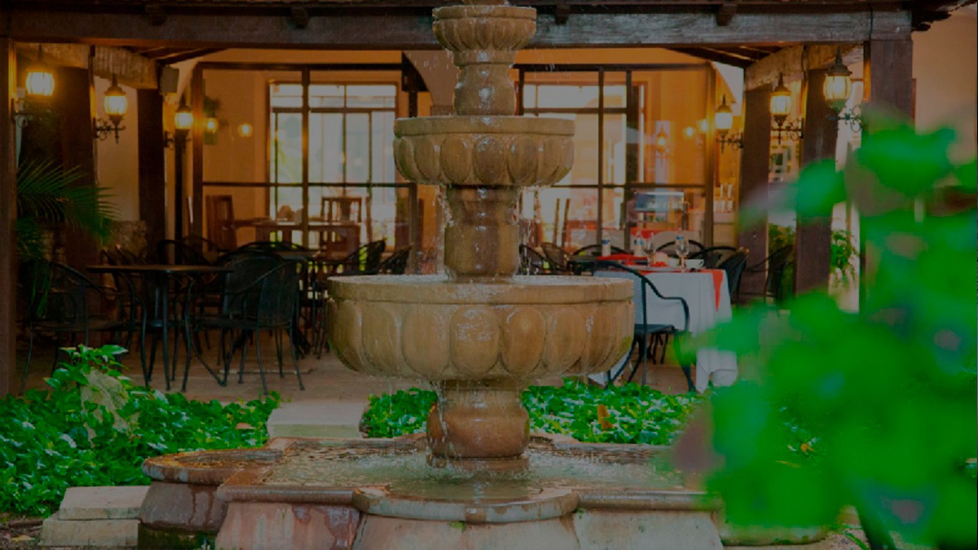 Fuente de piedra ornamentada en un patio, con asientos de restaurante visibles al fondo.