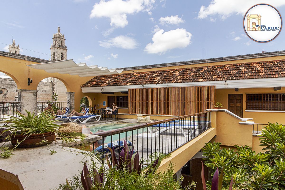 Piscina y patio en la azotea de un edificio amarillo con arcos, día soleado.