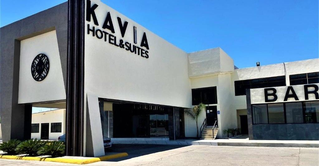 Entrada al Kavia Hotel & Suites, edificio blanco con bar, vista exterior soleada.