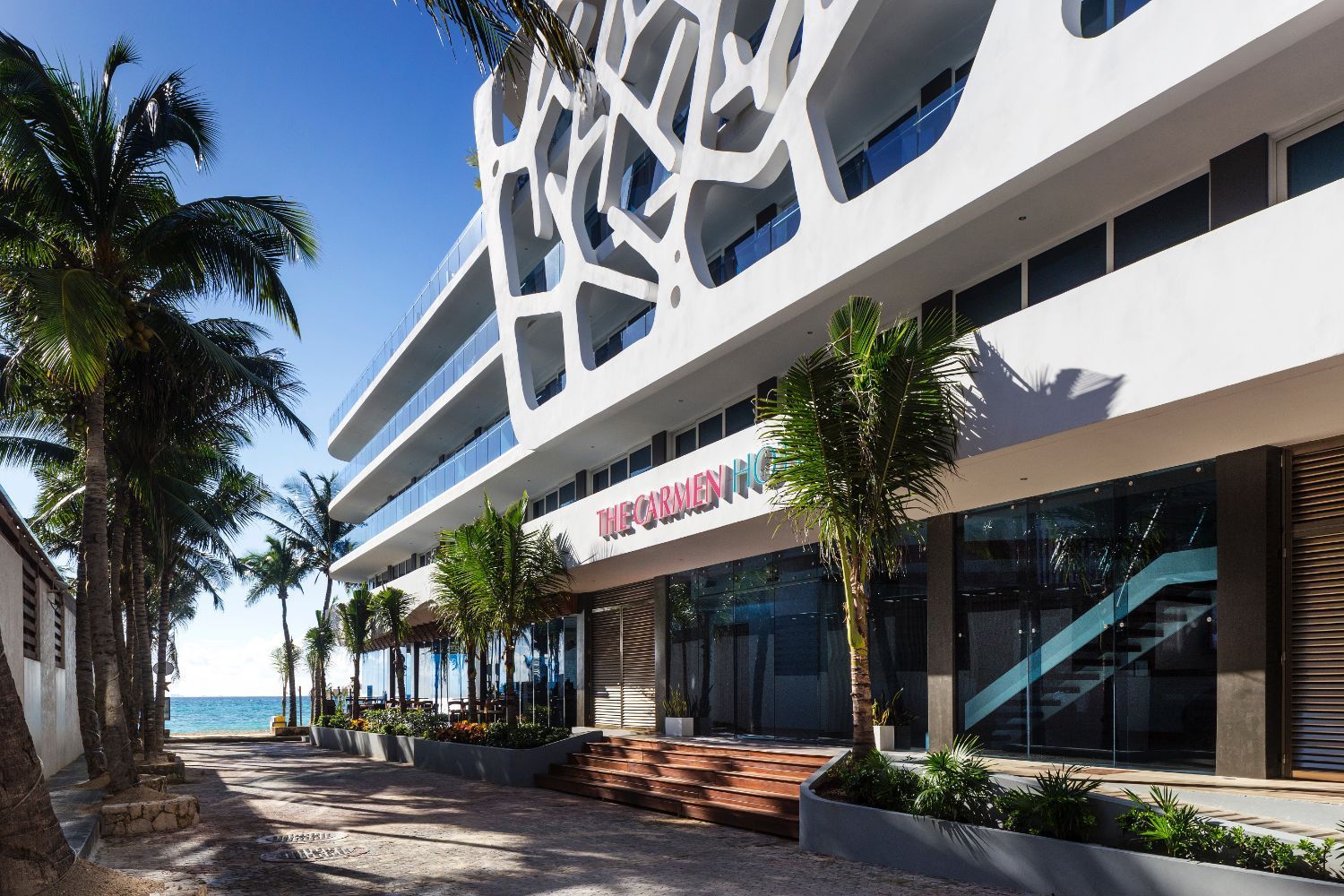 Moderno hotel blanco con fachada intrincada, palmeras y vista al mar.