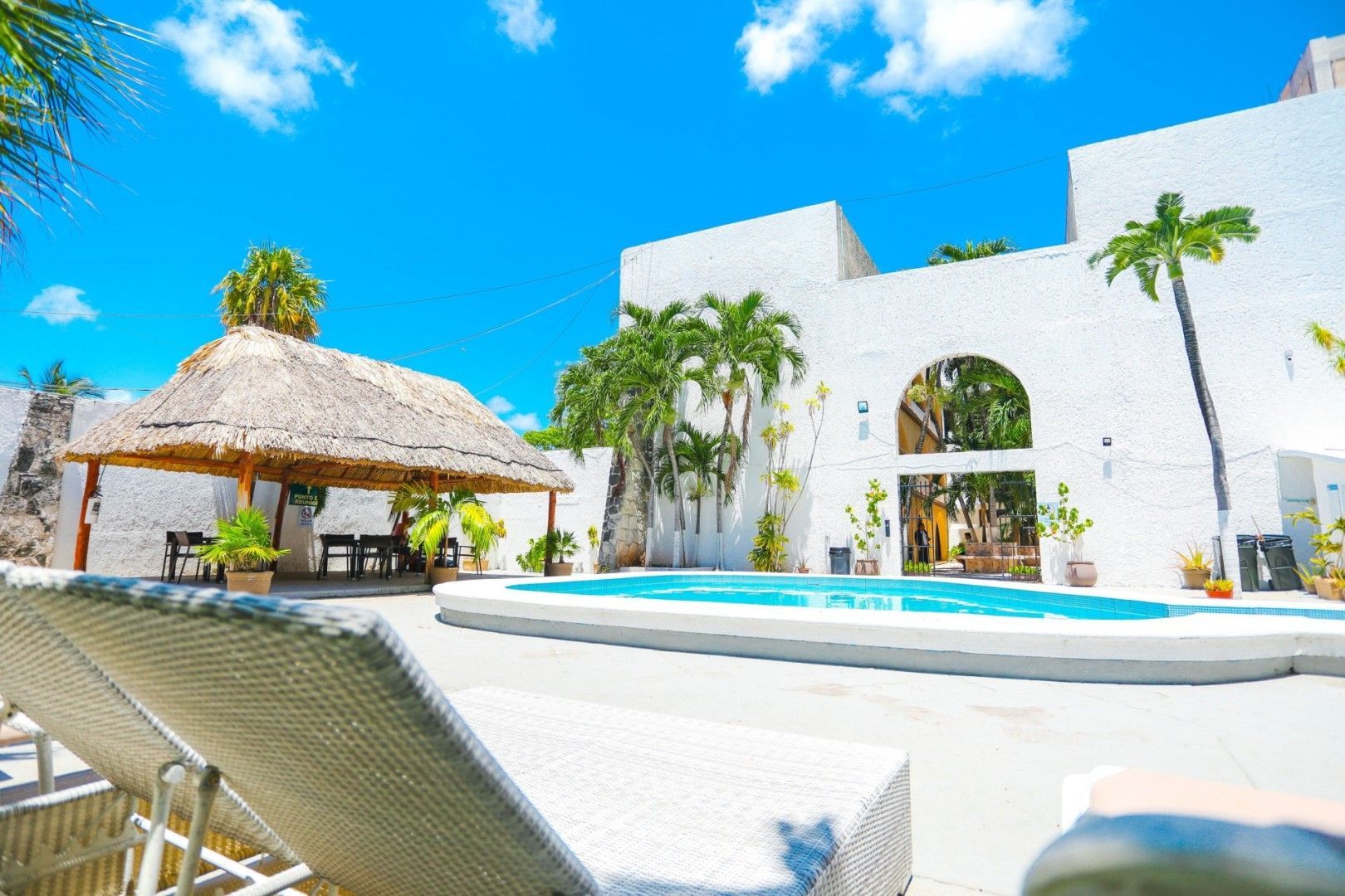 Zona de piscina con edificios blancos, techo de paja y cielo azul.