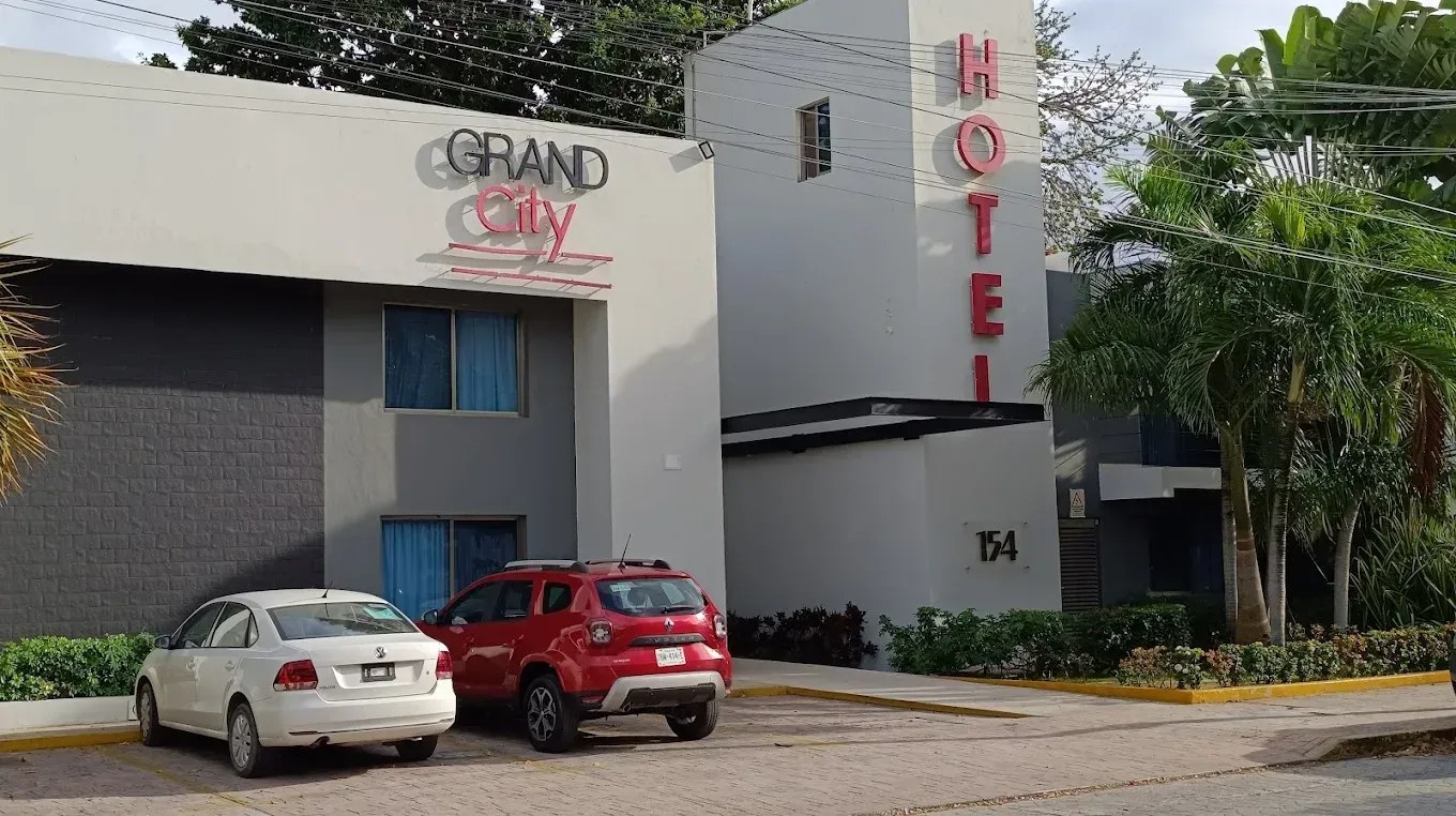 Edificio del hotel “Grand City” con señalización roja y blanca; coches aparcados delante.