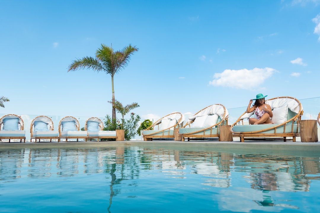 Piscina con camastros, vista al mar, cielo azul y una persona relajándose.