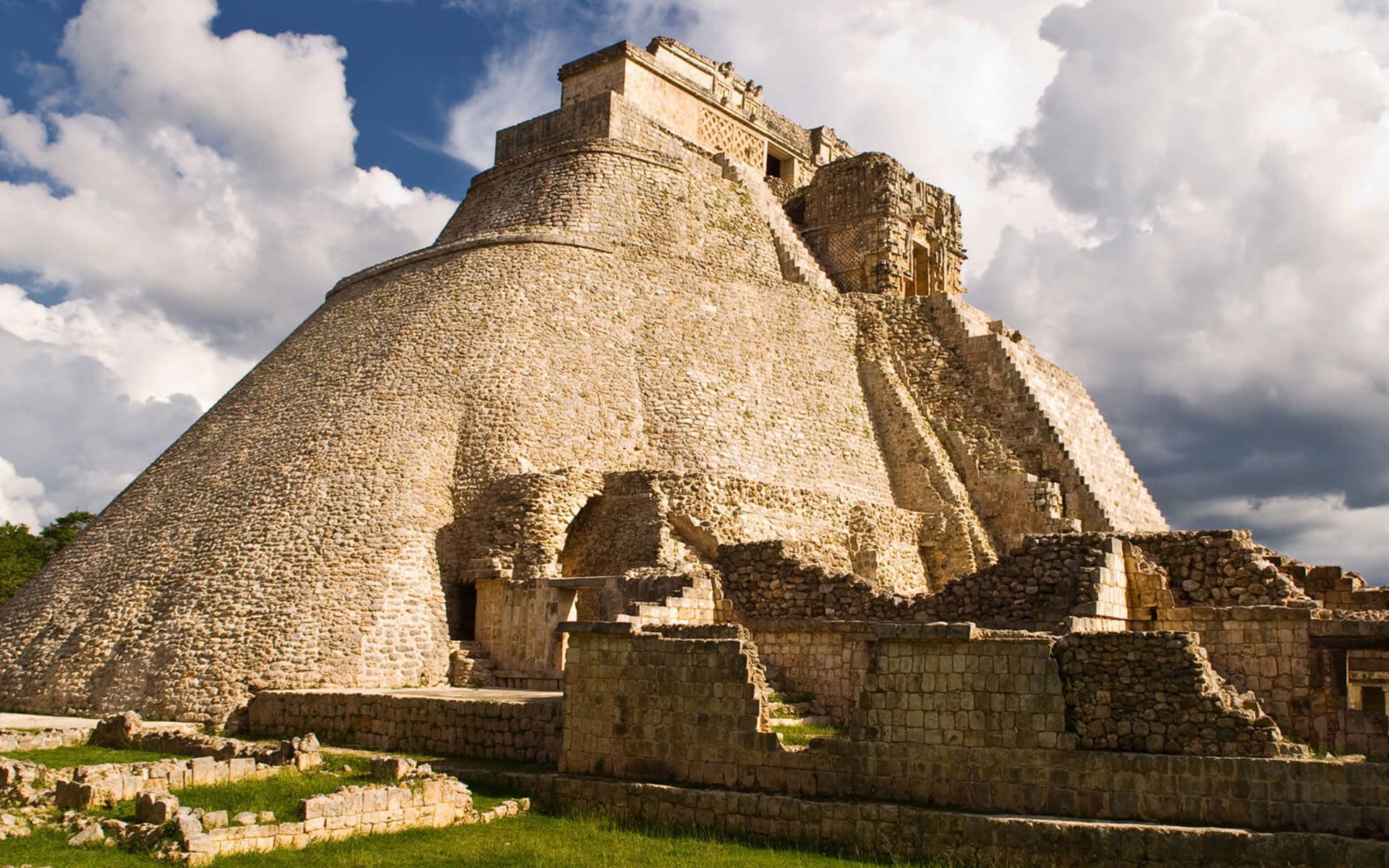 La Pirámide del Adivino en Uxmal, México, una enorme estructura de piedra con esquinas redondeadas que se recorta contra un cielo azul nublado.