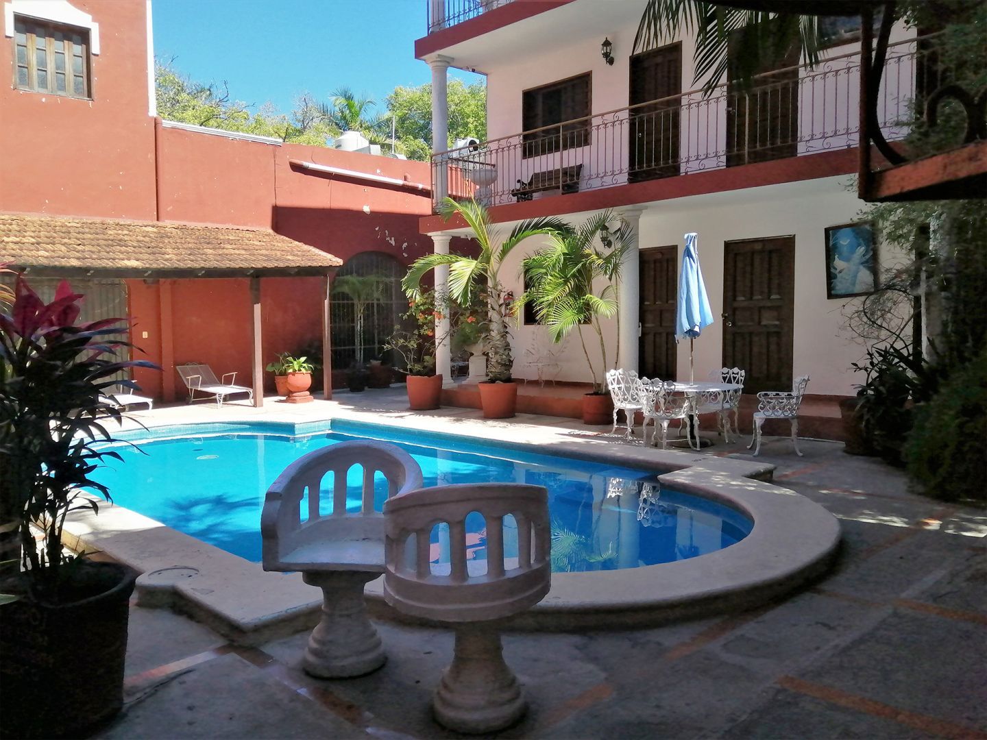 Área de piscina con piscina color turquesa, sillas blancas y un edificio de dos pisos al fondo.